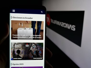 Stuttgart, Almanya - 04-09-2025: Ekvador televizyon kanalı Teleamazonas 'ın web sayfası ile logo önünde cep telefonu tutan kişi. Telefon ekranının merkezine odaklan.