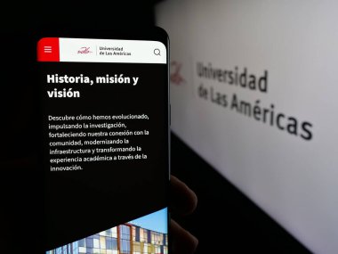 Stuttgart, Almanya - 04-09-2025: Üniversite Universidad de las Americas 'ın (UDLA) web sayfası logonun önünde cep telefonu tutan kişi. Telefon ekranının merkezine odaklan.