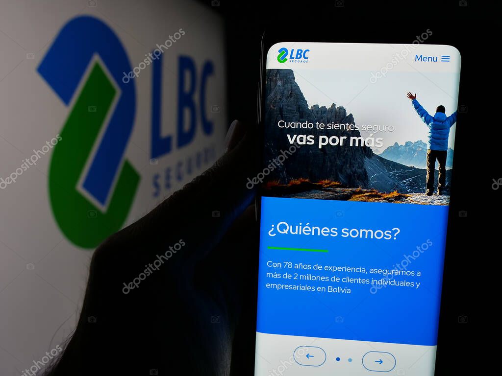 Stuttgart, Germany - 04-09-2025: Person holding cellphone with web page of Bolivian insurance company LBC Seguros on screen in front of logo. Focus on center of phone display.