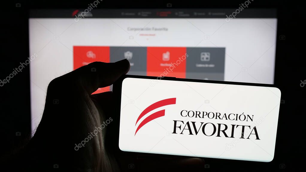 Stuttgart, Germany - 04-09-2025: Person holding mobile phone with logo of retail company Corporacion Favorita C.A. on screen in front of web page. Focus on phone display.