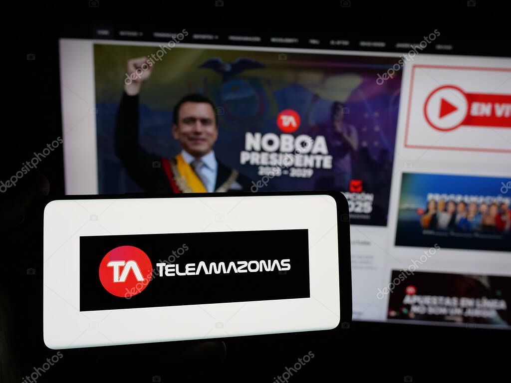Stuttgart, Germany - 04-09-2025: Person holding smartphone with logo of Ecuadorian television network Teleamazonas on screen in front of website. Focus on phone display.