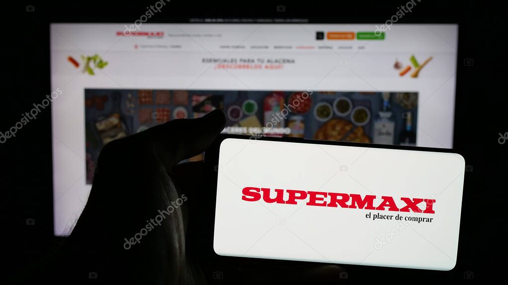 Stuttgart, Germany - 04-09-2025: Person holding mobile phone with logo of Ecuadorian retail company Supermaxi on screen in front of web page. Focus on phone display.