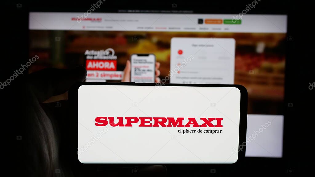 Stuttgart, Germany - 04-09-2025: Person holding cellphone with logo of Ecuadorian retail company Supermaxi on screen in front of webpage. Focus on phone display.