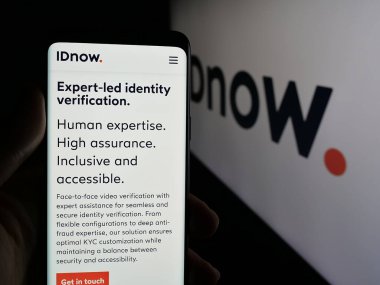 Stuttgart, Almanya - 04-17-2025: Cep telefonunda kimlik doğrulama şirketi IDnow GmbH 'nin web sayfası bulunan kişi logonun önünde ekranda. Telefon ekranının merkezine odaklan.