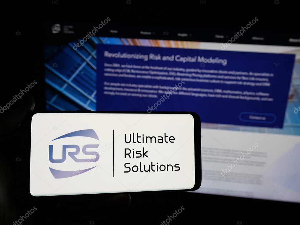 Stuttgart, Germany - 04-17-2025: Person holding smartphone with logo of US company Ultimate Risk Solutions (URS) on screen in front of website. Focus on phone display.