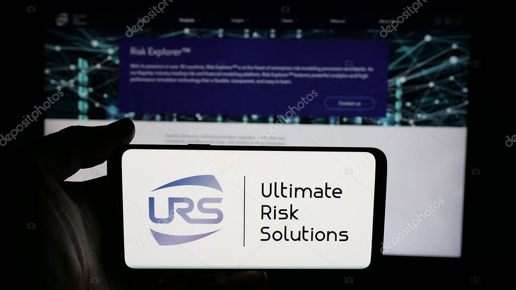 Stuttgart, Germany - 04-17-2025: Person holding cellphone with logo of US company Ultimate Risk Solutions (URS) on screen in front of webpage. Focus on phone display.