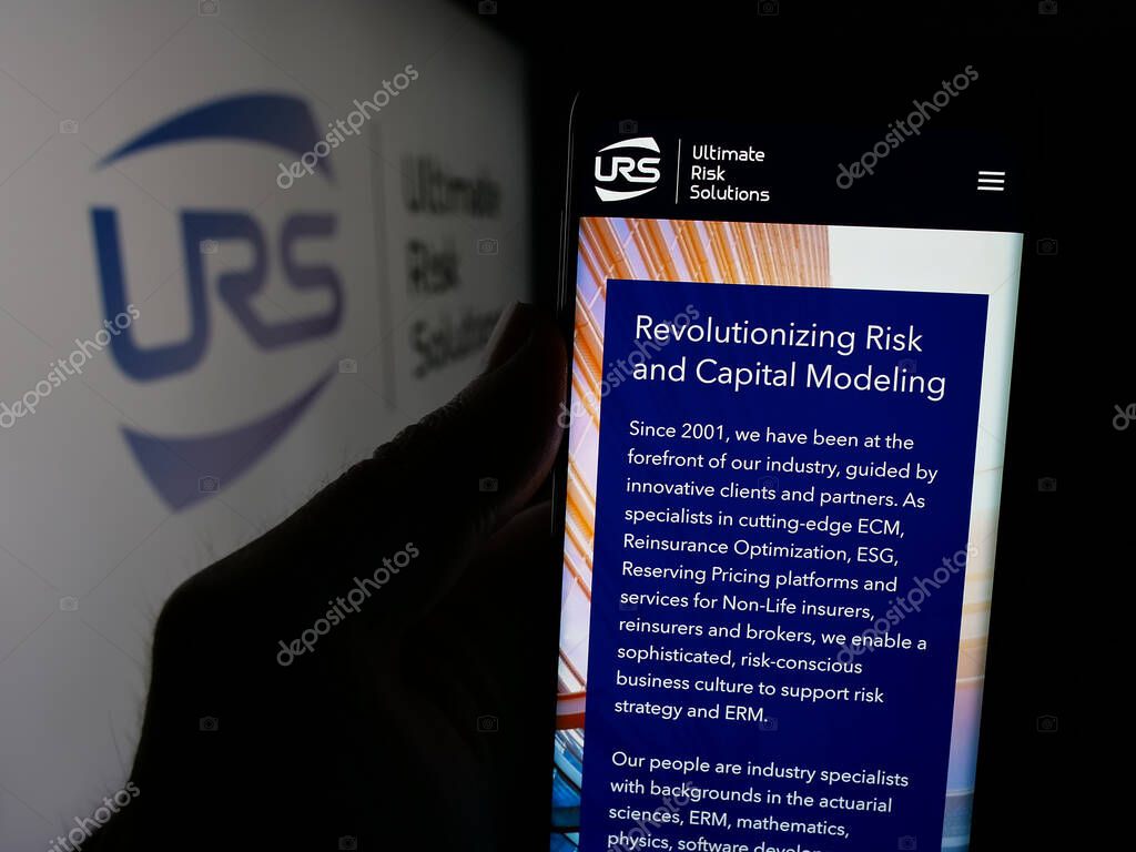 Stuttgart, Germany - 04-17-2025: Person holding cellphone with web page of US company Ultimate Risk Solutions (URS) on screen in front of logo. Focus on center of phone display.