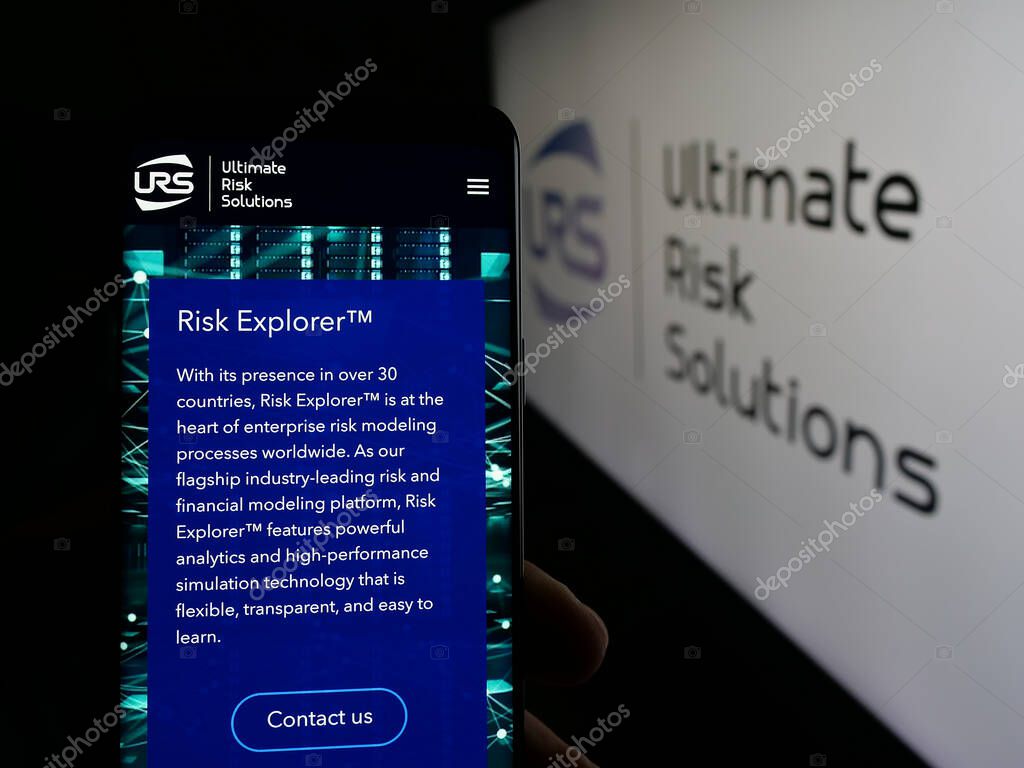 Stuttgart, Germany - 04-17-2025: Person holding smartphone with website of US company Ultimate Risk Solutions (URS) on screen in front of logo. Focus on center of phone display.