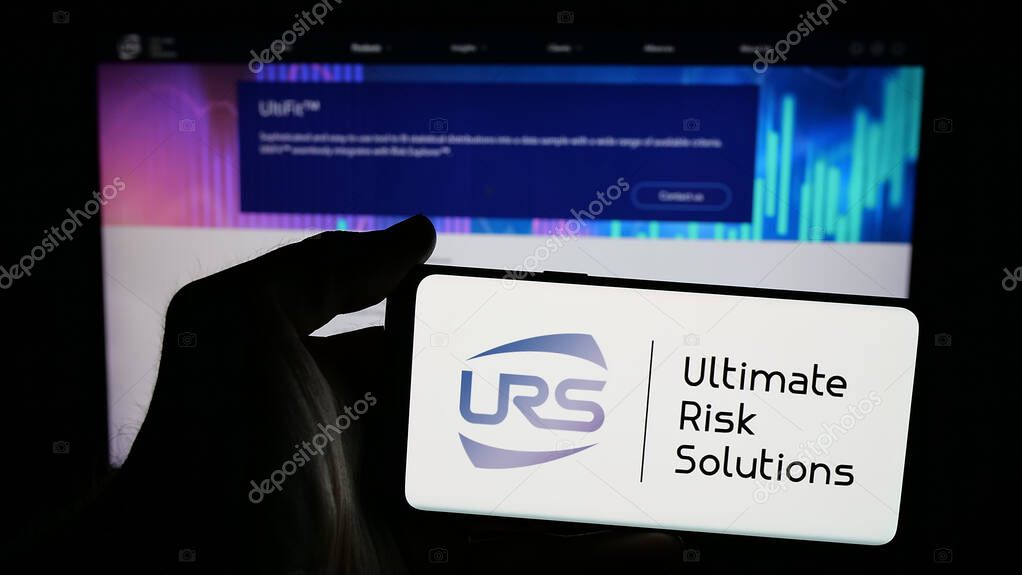 Stuttgart, Germany - 04-17-2025: Person holding mobile phone with logo of US company Ultimate Risk Solutions (URS) on screen in front of web page. Focus on phone display.