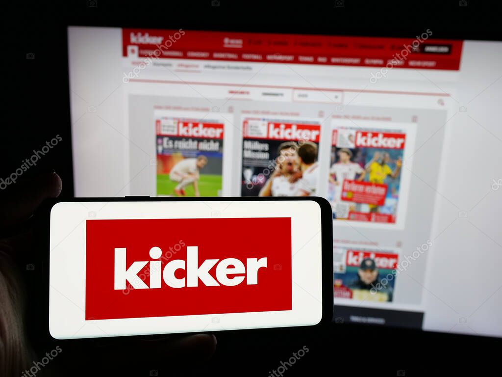 Stuttgart, Germany - 04-17-2025: Person holding smartphone with logo of German football and sports magazine Kicker on screen in front of website. Focus on phone display.