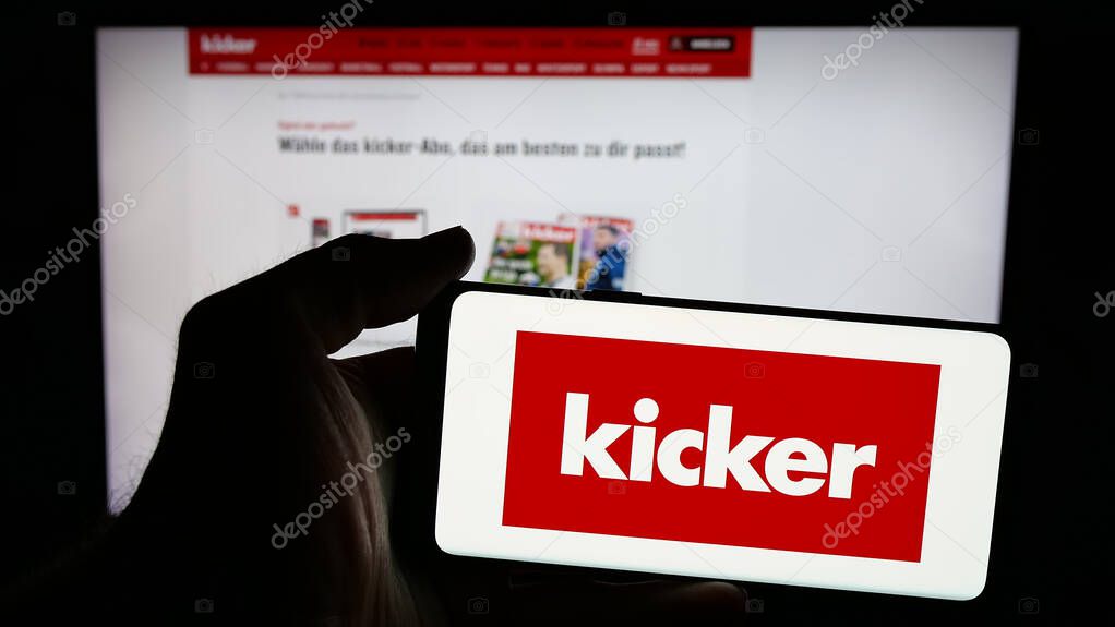 Stuttgart, Germany - 04-17-2025: Person holding mobile phone with logo of German football and sports magazine Kicker on screen in front of web page. Focus on phone display.