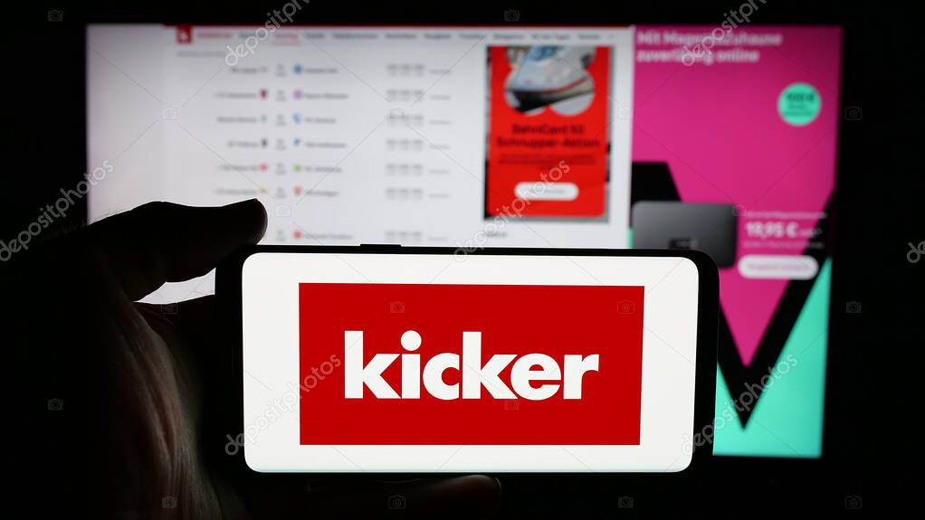 Stuttgart, Germany - 04-17-2025: Person holding cellphone with logo of German football and sports magazine Kicker on screen in front of webpage. Focus on phone display.