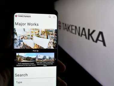 Stuttgart, Almanya - 04-24-2025: İnşaat şirketi Takenaka Corporation 'ın web sitesi ile birlikte logo önünde akıllı telefon tutan kişi. Telefon ekranının merkezine odaklan.