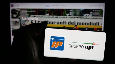 Stuttgart, Almanya - 04-24-2025: İnternet sayfası önünde ekranda Italiana Petroli S.p.A. (Gruppo API) şirketinin logosuna sahip cep telefonu bulunduran kişi. Telefon ekranına odaklan.