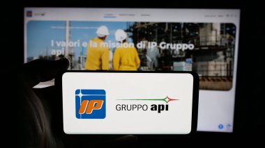 Stuttgart, Almanya - 04-24-2025: İnternet sayfası önünde ekranda Italiana Petroli S.p.A. (Gruppo API) şirketinin logosunun bulunduğu cep telefonu sahibi kişi. Telefon ekranına odaklan.