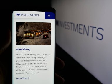 Stuttgart, Almanya - 04-24-2025: Logo önünde SM Investments Corporation (SMIC) şirketinin web sitesi ile akıllı telefonu elinde tutan kişi. Telefon ekranının merkezine odaklan.