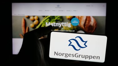 Stuttgart, Almanya - 04-24-2025: Norveç toptan satış şirketi NorgesGruppen ASA 'nın logosuna sahip cep telefonu sahibi kişi web sayfası önünde ekranda. Telefon ekranına odaklan.