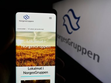 Stuttgart, Almanya - 04-24-2025: Norveçli toptan satış şirketi NorgesGruppen ASA 'nın web sayfası ile cep telefonu tutan kişi logonun önünde ekranda. Telefon ekranının merkezine odaklan.