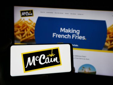 Stuttgart, Almanya - 04-24-2025: Kanadalı gıda şirketi McCain Foods Limited 'in logosuna sahip akıllı telefon sahibi kişi web sitesinin önünde ekranda. Telefon ekranına odaklan.