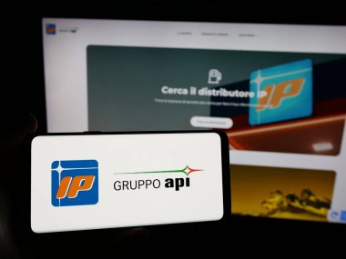 Stuttgart, Almanya - 04-24-2025: İnternet sitesinin önünde üzerinde Italiana Petroli S.p.A. (Gruppo API) şirketinin logosu bulunan akıllı telefon sahibi kişi. Telefon ekranına odaklan.