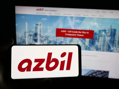 Stuttgart, Almanya - 04-25-2025: Japon otomasyon şirketi Azbil Corporation 'ın logosunu elinde tutan kişi web sitesinin önünde ekranda. Telefon ekranına odaklan.