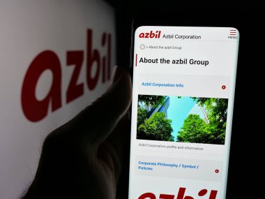 Stuttgart, Almanya - 04-25-2025: Japon otomasyon şirketi Azbil Corporation 'ın web sitesi ile birlikte logo önünde akıllı telefon tutan kişi. Telefon ekranının merkezine odaklan.