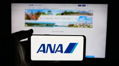 Stuttgart, Almanya - 04-25-2025: Web sayfası önünde All Nippon Airways Co. Ltd. (ANA) şirketinin logosunun bulunduğu cep telefonu sahibi kişi. Telefon ekranına odaklan.