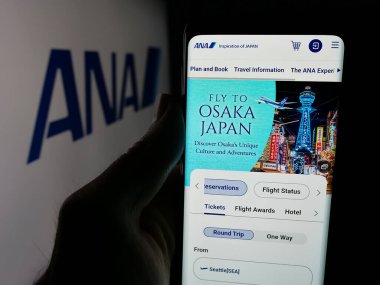 Stuttgart, Almanya - 04-25-2025: Logonun önündeki ekranda All Nippon Airways Co. Ltd. (ANA) şirketinin web sayfası bulunan kişi. Telefon ekranının merkezine odaklan.