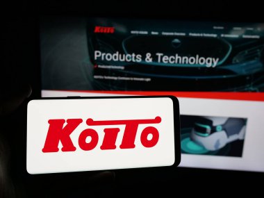 Stuttgart, Almanya - 04-25-2025: Japon şirketi Koito Manufacturing Co. Ltd. nin logosuna sahip akıllı telefon sahibi kişi web sitesinin önünde ekranda. Telefon ekranına odaklan.