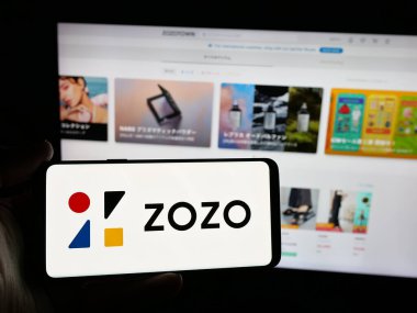 Stuttgart, Almanya - 04-25-2025: İnternet sitesinin önünde üzerinde Japon e-ticaret şirketi ZOZO Inc. 'nin logosu bulunan akıllı telefon sahibi kişi. Telefon ekranına odaklan.