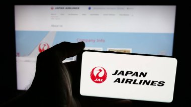 Stuttgart, Almanya - 04-25-2025: İnternet sayfasının önündeki ekranda Japon Airlines Co. Ltd. (JAL) havayolu şirketinin logosunun bulunduğu cep telefonu sahibi kişi. Telefon ekranına odaklan.