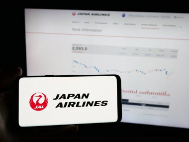 Stuttgart, Almanya - 04-25-2025: İnternet sitesinin önünde üzerinde Japon Havayolları Co. Ltd. (JAL) adlı havayolu şirketinin logosunun bulunduğu akıllı telefon bulunan kişi. Telefon ekranına odaklan.