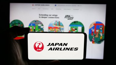 Stuttgart, Almanya - 04-25-2025: İnternet sayfası önünde Japon Airlines Co. Ltd. (JAL) adlı havayolu şirketinin logosuyla cep telefonu bulunduran kişi. Telefon ekranına odaklan.