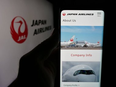 Stuttgart, Almanya - 04-25-2025: Havayolu şirketi Japan Airlines Co. Ltd. (JAL) 'in web sayfası logonun önünde bulunan kişi. Telefon ekranının merkezine odaklan.
