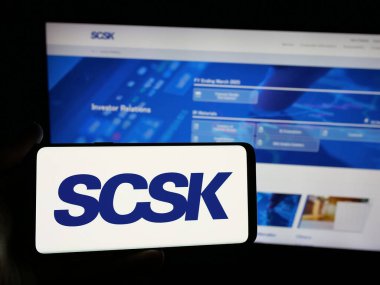 Stuttgart, Almanya - 04-25-2025: Japon bilişim şirketi SCSK Corporation 'ın logosunu elinde tutan kişi web sitesinin önünde ekranda. Telefon ekranına odaklan.
