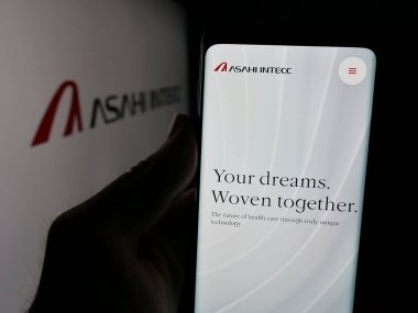 Stuttgart, Almanya - 04-25-2025: Japon şirketi ASAHI INTECC Co. Ltd. nin web sayfası ile cep telefonu tutan kişi logonun önünde ekranda. Telefon ekranının merkezine odaklan.