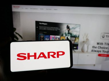 Stuttgart, Almanya - 04-26-2025: İnternet sitesinin önünde üzerinde elektronik şirketi Sharp Corporation 'ın logosu olan akıllı telefonu tutan kişi. Telefon ekranına odaklan.