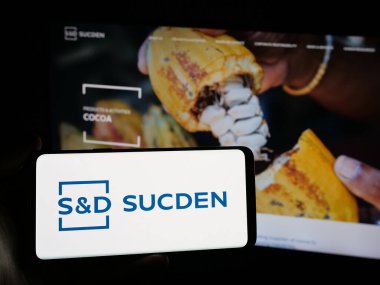Stuttgart, Almanya - 04-26-2025: İnternet sitesi önünde üzerinde Fransız şirketi Sucres et Denrees 'in (Sucden) logosu bulunan akıllı telefon sahibi kişi. Telefon ekranına odaklan.