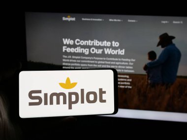 Stuttgart, Almanya - 04-26-2025: ABD 'li tarım şirketi J. R. Simplot Company' nin logosunu elinde tutan kişi web sitesinin önünde ekranda. Telefon ekranına odaklan.