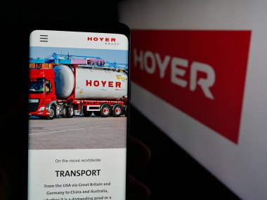 Stuttgart, Almanya - 04-26-2025: Lojistik şirketi Wilhelm Hoyer B.V. Co. KG 'nin web sayfası logonun önünde duran kişi. Telefon ekranının merkezine odaklan.