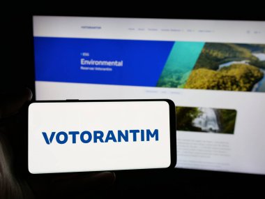 Stuttgart, Almanya - 04-26-2025: Brezilyalı yatırım şirketi Votorantim S.A. 'nın logosunu elinde tutan kişi web sitesinin önünde ekranda. Telefon ekranına odaklan.