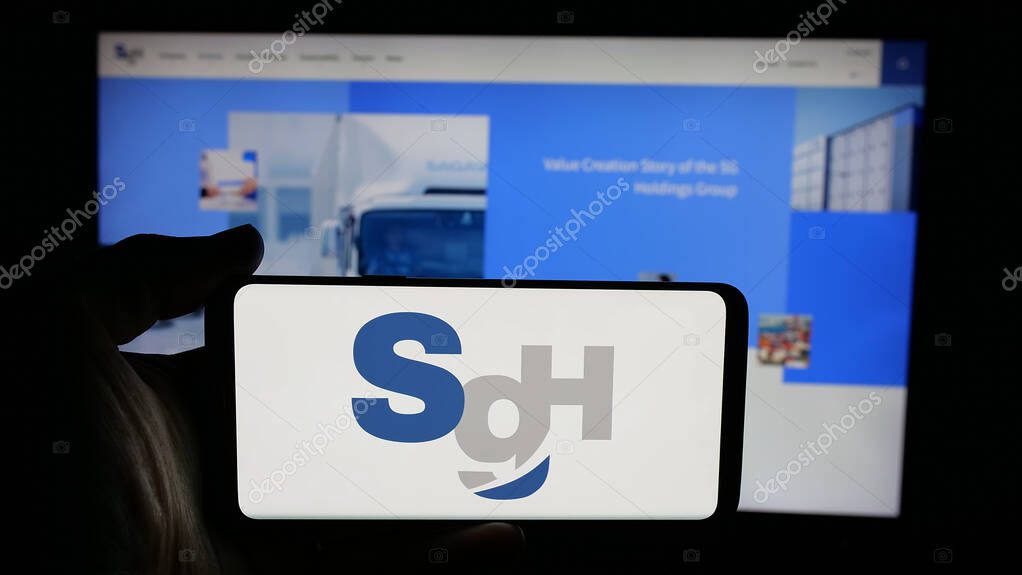 Stuttgart, Germany - 04-26-2025: Person holding cellphone with logo of logistics company SG Holdings Co. Ltd. on screen in front of webpage. Focus on phone display.