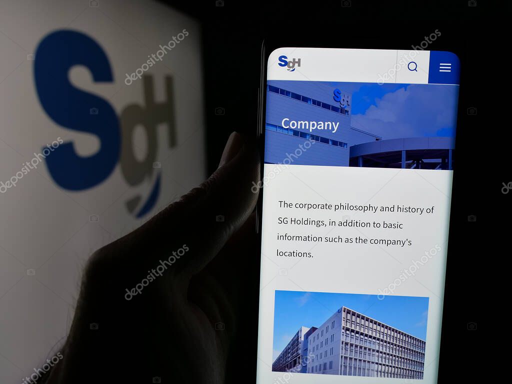 Stuttgart, Germany - 04-26-2025: Person holding smartphone with website of logistics company SG Holdings Co. Ltd. on screen in front of logo. Focus on center of phone display.