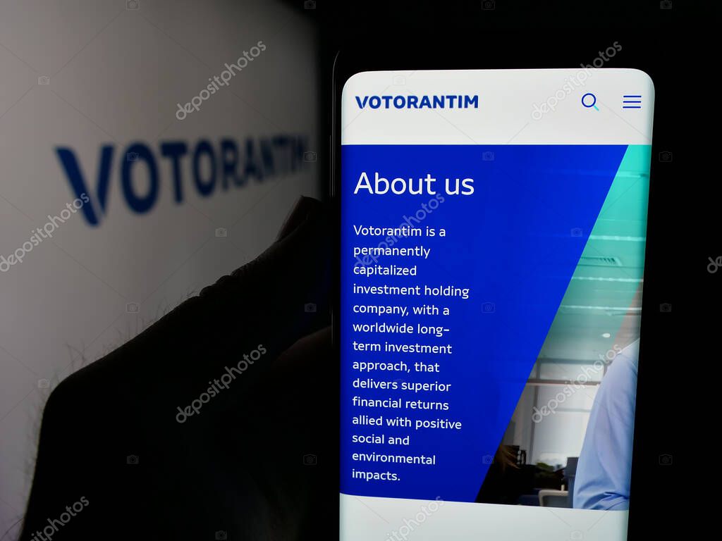 Stuttgart, Germany - 04-26-2025: Person holding smartphone with website of Brazilian investment company Votorantim S.A. on screen in front of logo. Focus on center of phone display.
