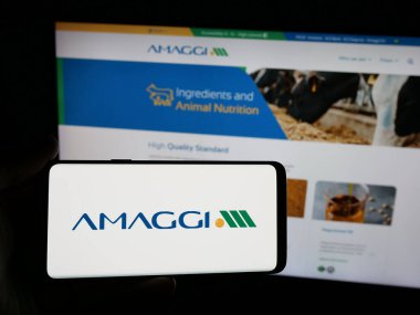 Stuttgart, Almanya - 04-28-2025: Brezilyalı tarım şirketi Amaggi Group 'un logosuna sahip akıllı telefonu web sitesinin önünde ekranda tutan kişi. Telefon ekranına odaklan.