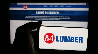 Stuttgart, Almanya - 05-02-2025: İnternet sayfası önünde üzerinde 84 Kereste Şirketi (84Lumber) logosu bulunan cep telefonu sahibi kişi. Telefon ekranına odaklan.