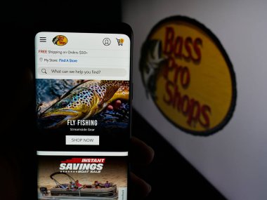 Stuttgart, Almanya - 05-02-2025: ABD 'li Bass Pro Shops (BPS Direct LLC) şirketinin web sayfası logo önünde bulunan kişi. Telefon ekranının merkezine odaklan.
