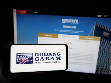 Stuttgart, Almanya - 05-02-2025: Endonezyalı tütün şirketi Gudang Garam 'ın logosunu elinde tutan kişi web sitesinin önünde ekranda. Telefon ekranına odaklan.