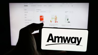 Stuttgart, Almanya - 05-02-2025: Web sayfası önünde ekranda ABD 'li çok katlı pazarlama şirketi Amway Corp' un logosunun bulunduğu cep telefonu sahibi kişi. Telefon ekranına odaklan.