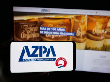 Stuttgart, Almanya - 05-03-2025: Web sitesinin önünde Azucarera Paraguaya S.A. (AZPA) şirketinin logosuna sahip akıllı telefonu elinde tutan kişi. Telefon ekranına odaklan.